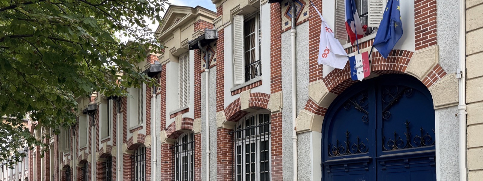 Façade de brique et de pierre du lycée Carnot, avec sa porte bleue et les drapeaux